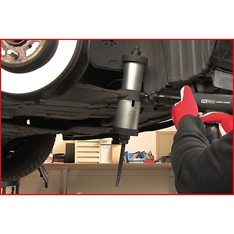 Mechaniker schraubt mit rotem Handschuh und KS TOOLS Werkzeug an Fahrzeug. Silberfarbenes Werkzeug an Radaufhängung.